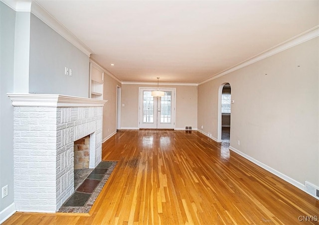 unfurnished living room with arched walkways, french doors, wood finished floors, and baseboards