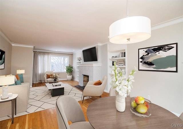 living room featuring light wood-style floors, crown molding, a fireplace, and built in features