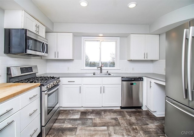 kitchen with appliances with stainless steel finishes, white cabinetry, a sink, and decorative backsplash