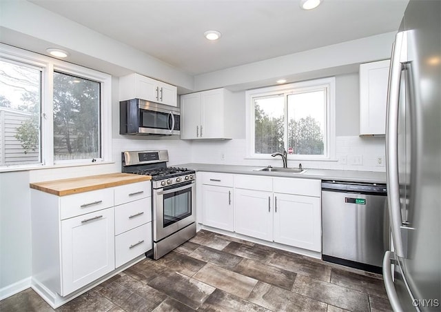 kitchen featuring a sink, white cabinetry, wooden counters, appliances with stainless steel finishes, and decorative backsplash