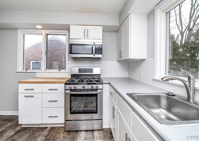 kitchen with appliances with stainless steel finishes, dark wood-style flooring, a sink, white cabinetry, and backsplash