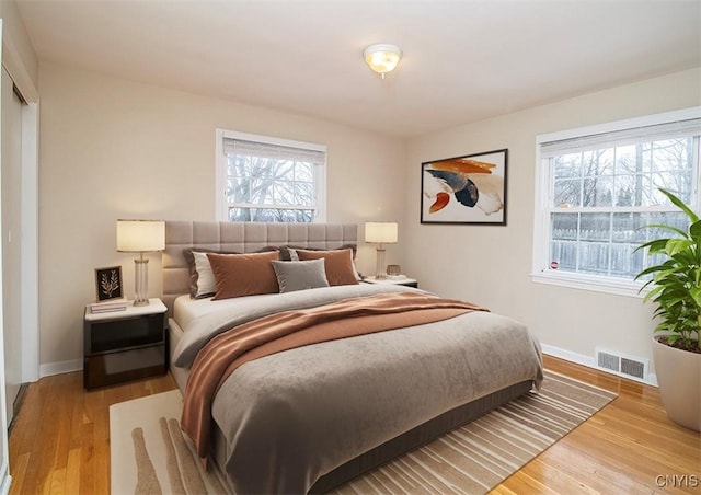 bedroom featuring baseboards, multiple windows, visible vents, and wood finished floors