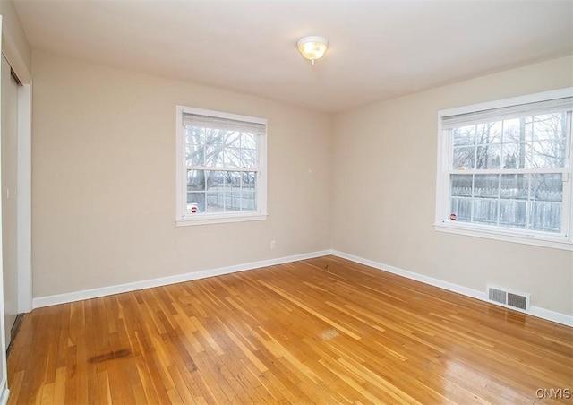 empty room with a wealth of natural light, light wood finished floors, visible vents, and baseboards