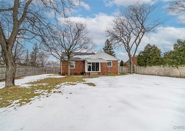 snow covered rear of property with brick siding and fence private yard