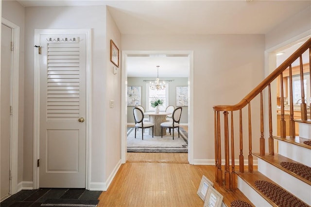 entryway featuring stairs, an inviting chandelier, wood finished floors, and baseboards