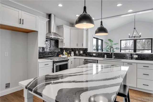 kitchen with light wood finished floors, lofted ceiling, stainless steel appliances, wall chimney range hood, and a sink