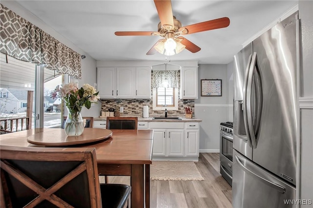 kitchen with appliances with stainless steel finishes, light wood-style floors, white cabinetry, and a sink