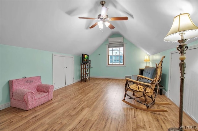 sitting room featuring a ceiling fan, baseboards, vaulted ceiling, light wood-type flooring, and a wall mounted air conditioner