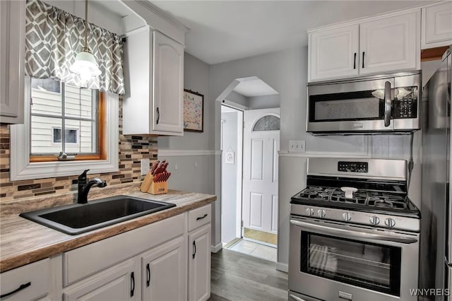 kitchen with stainless steel appliances, arched walkways, white cabinetry, and a sink