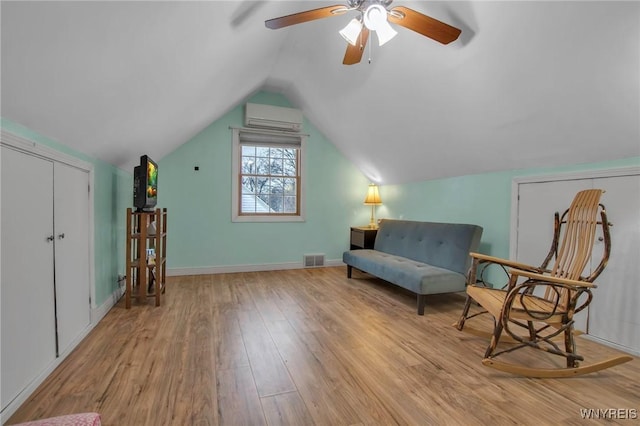 sitting room featuring visible vents, an AC wall unit, vaulted ceiling, wood finished floors, and baseboards