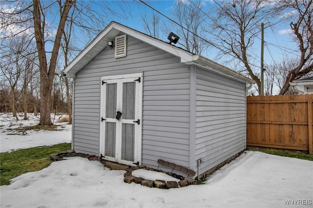 snow covered structure with a storage shed, fence, and an outdoor structure