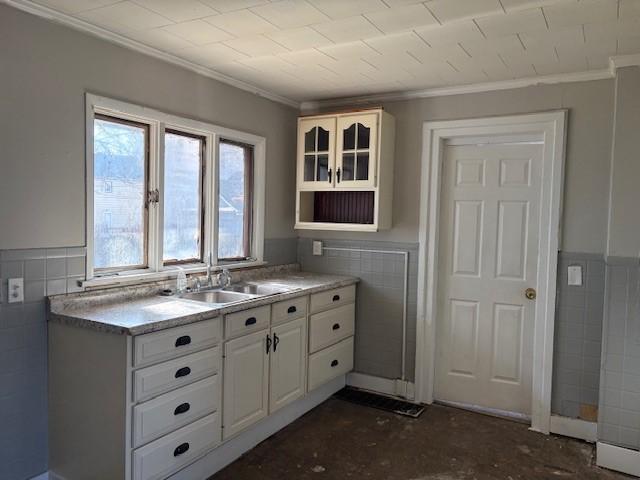 kitchen with a sink, tile walls, white cabinets, wainscoting, and crown molding