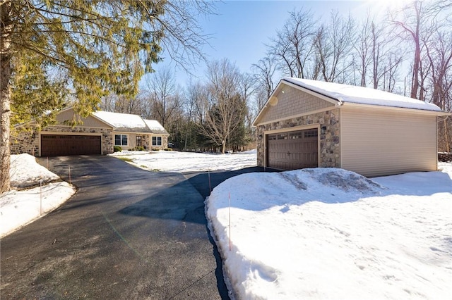 view of snowy exterior featuring stone siding, a detached garage, and an outdoor structure