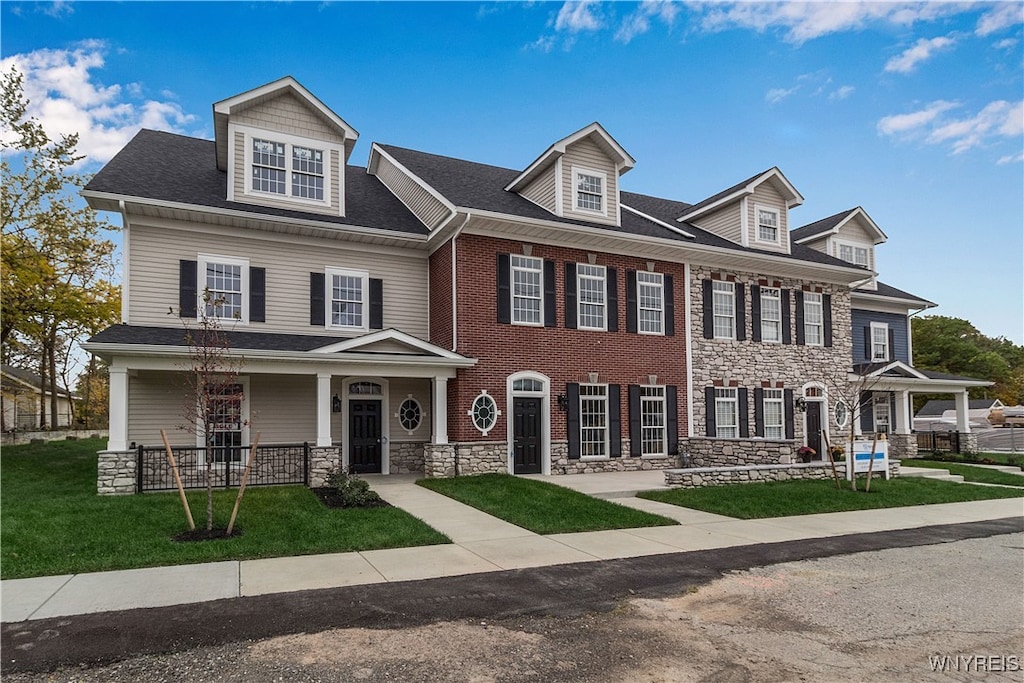 view of front of home featuring stone siding, covered porch, brick siding, and a front lawn