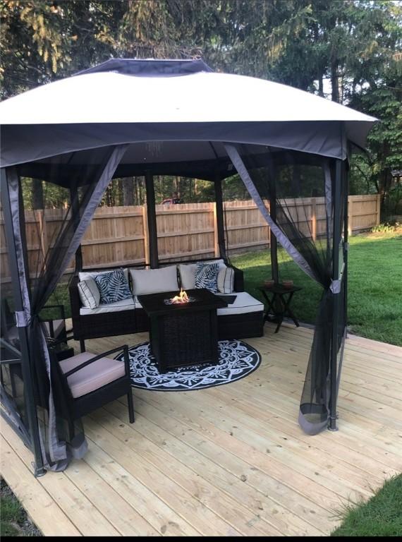 deck featuring an outdoor living space with a fire pit, a fenced backyard, a lawn, and a gazebo