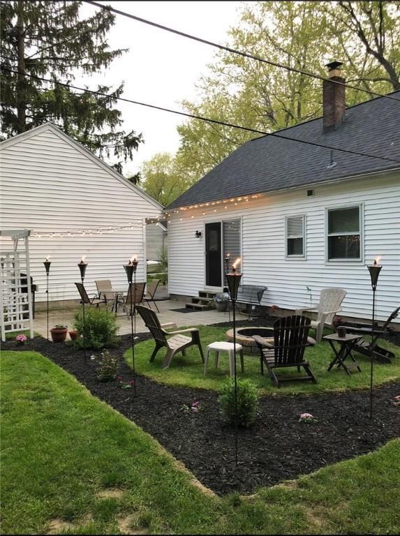 back of property with entry steps, a shingled roof, a lawn, a chimney, and a patio area