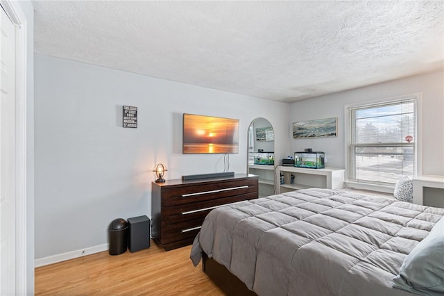 bedroom featuring light wood finished floors, baseboards, arched walkways, and a textured ceiling