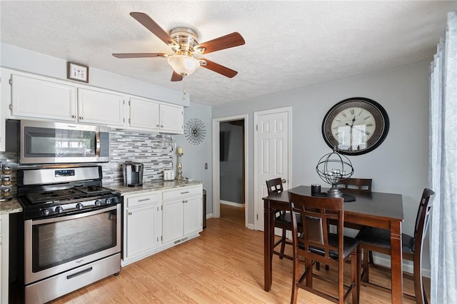 kitchen with appliances with stainless steel finishes, light wood-type flooring, white cabinets, and backsplash