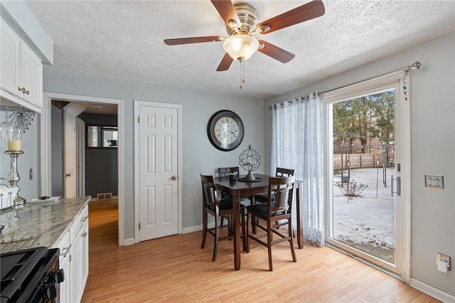 dining area with a textured ceiling, light wood-type flooring, visible vents, and baseboards