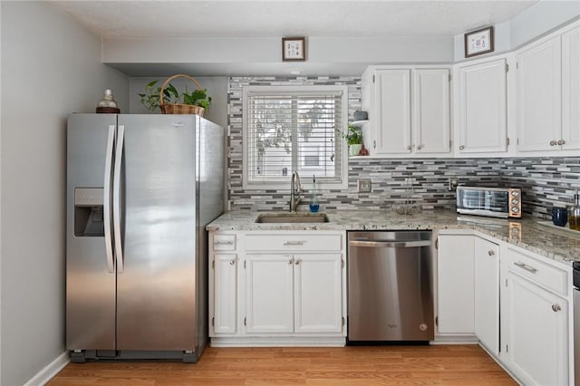 kitchen featuring stainless steel appliances, a sink, white cabinetry, light wood-type flooring, and tasteful backsplash