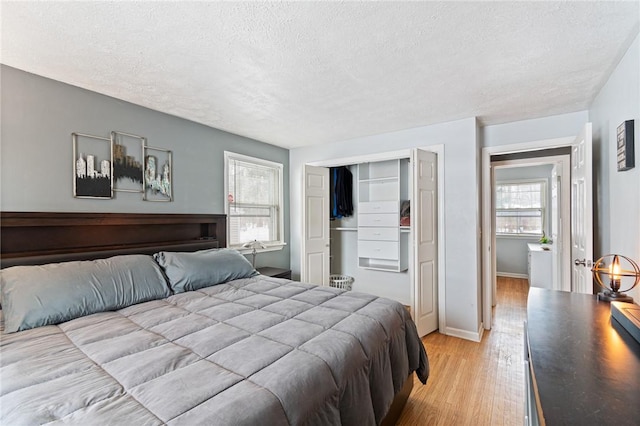 bedroom with a closet, baseboards, a textured ceiling, and light wood finished floors