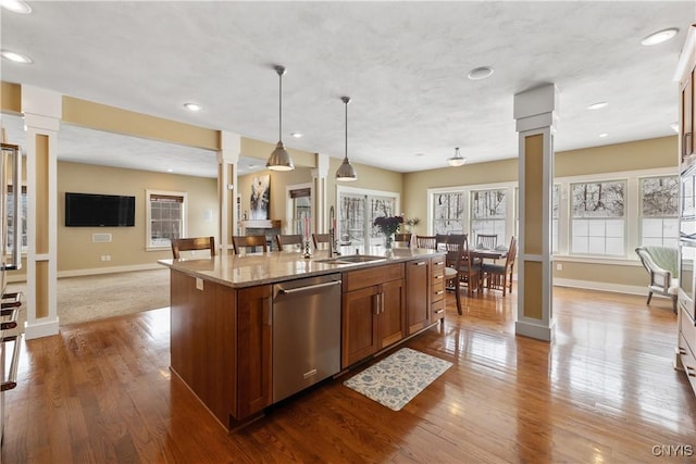 kitchen with a kitchen island with sink, dishwasher, a sink, and decorative columns