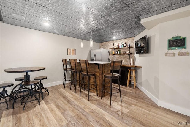 bar featuring baseboards, bar, stainless steel fridge with ice dispenser, and wood finished floors