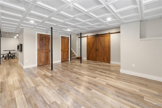 below grade area with a barn door, light wood-type flooring, and baseboards