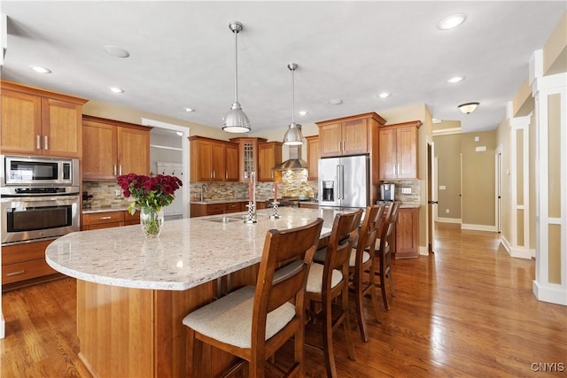 kitchen with brown cabinetry, wood finished floors, stainless steel appliances, a kitchen bar, and backsplash