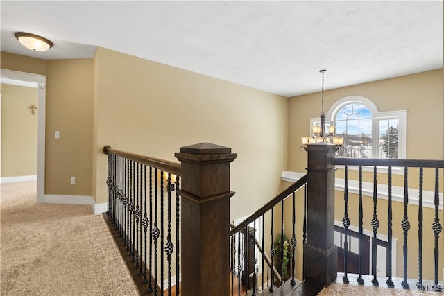 hallway with carpet floors, a chandelier, baseboards, and an upstairs landing