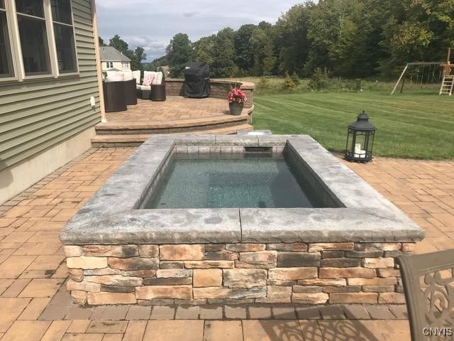 view of pool with an in ground hot tub, a playground, a patio, and a lawn