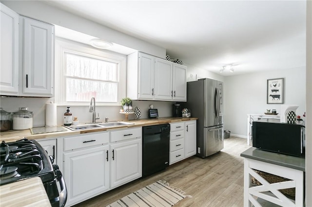 kitchen featuring butcher block countertops, a sink, white cabinetry, light wood-type flooring, and black appliances