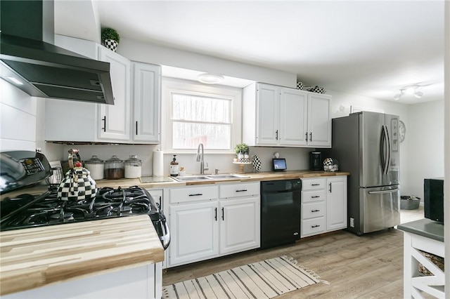 kitchen with wooden counters, white cabinets, a sink, black appliances, and wall chimney exhaust hood