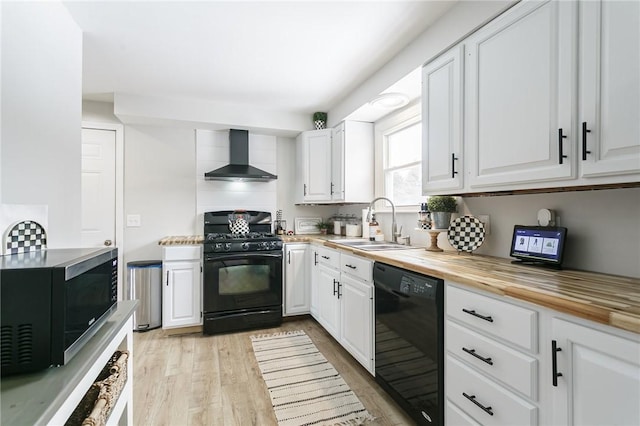 kitchen featuring white cabinetry, a sink, wood counters, wall chimney range hood, and black appliances