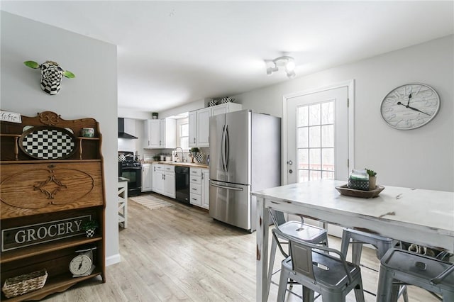 kitchen with light countertops, light wood-style floors, a sink, black appliances, and wall chimney exhaust hood