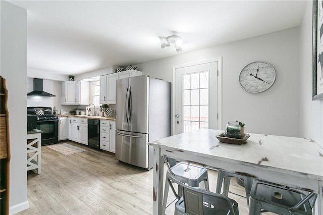 kitchen with light countertops, a sink, wall chimney range hood, light wood-type flooring, and black appliances