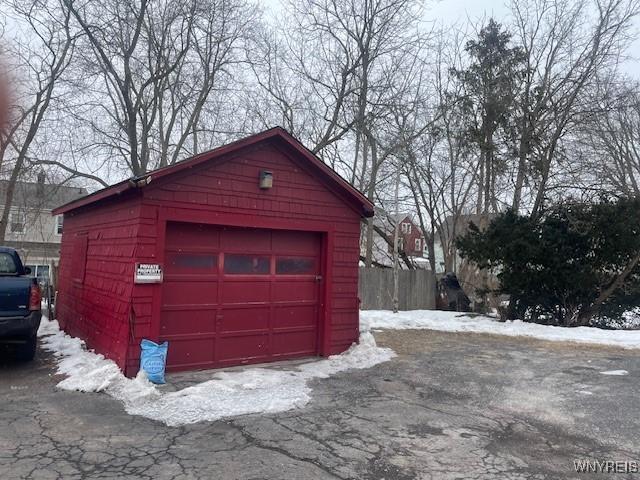 snow covered garage with driveway, a detached garage, and fence