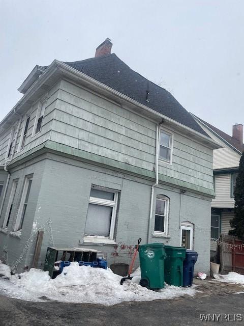 snow covered back of property with brick siding and a chimney