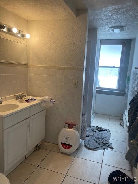 bathroom featuring a textured wall, tile patterned floors, a textured ceiling, vanity, and tile walls