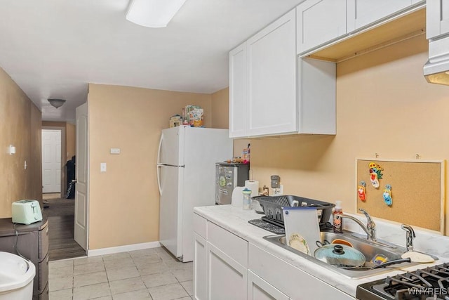 kitchen with light tile patterned floors, baseboards, freestanding refrigerator, light countertops, and white cabinetry