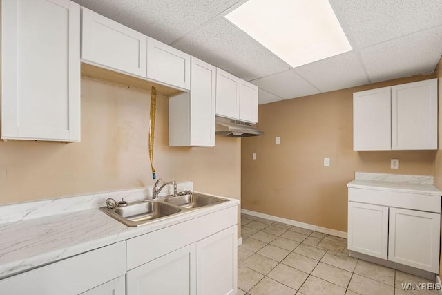 kitchen featuring light countertops, a paneled ceiling, under cabinet range hood, white cabinetry, and a sink