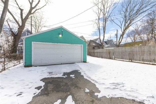 snow covered garage featuring a detached garage and fence