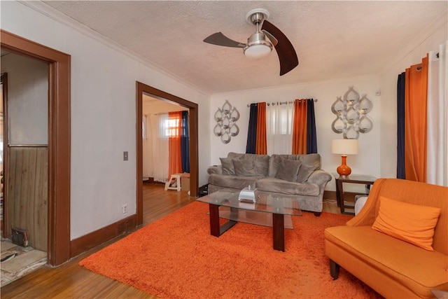 living room featuring a textured ceiling, wood finished floors, a ceiling fan, baseboards, and crown molding