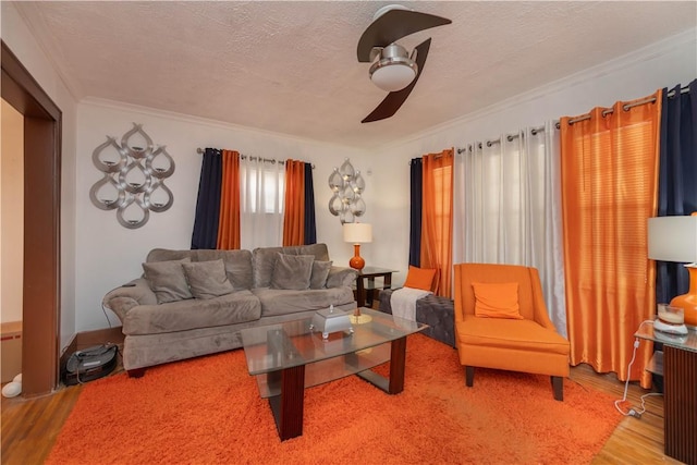 living room featuring a ceiling fan, a textured ceiling, ornamental molding, and wood finished floors