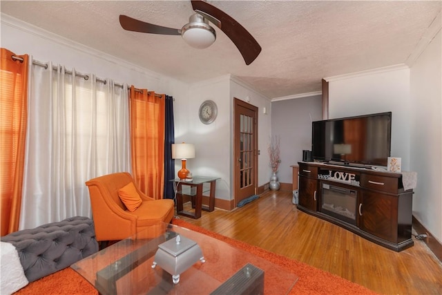 living area with baseboards, ceiling fan, wood finished floors, crown molding, and a textured ceiling