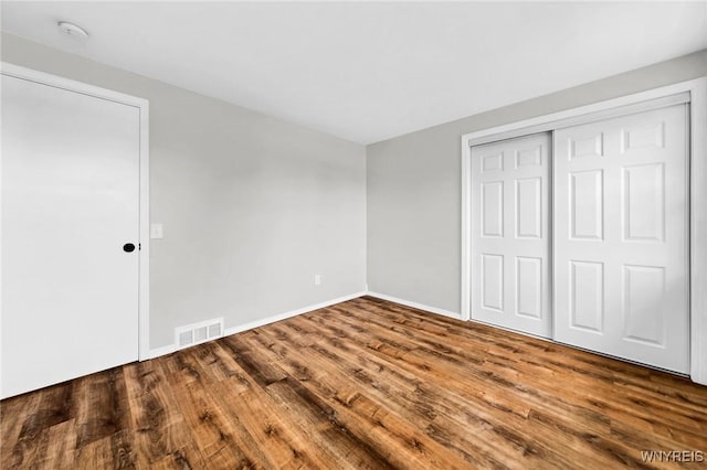 unfurnished bedroom with a closet, visible vents, baseboards, and wood finished floors