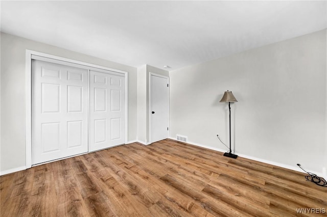 unfurnished bedroom featuring a closet, wood finished floors, visible vents, and baseboards