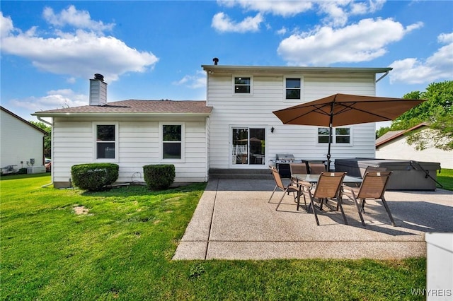 back of property featuring a yard, a chimney, a patio area, and a hot tub