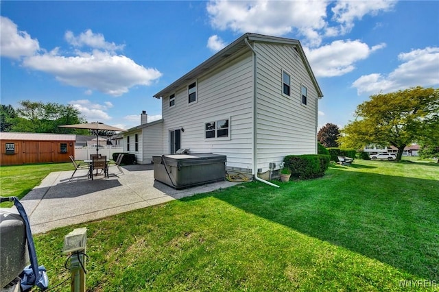 back of house with a yard, a hot tub, an outbuilding, and a patio