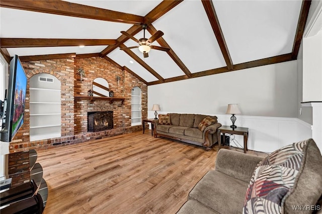 living room with built in features, a ceiling fan, lofted ceiling with beams, wood finished floors, and a fireplace